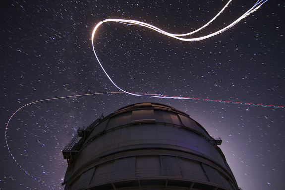 A long-exposure shot showing the wingsuit jumpers in their bright LED suits zooming across the night sky.